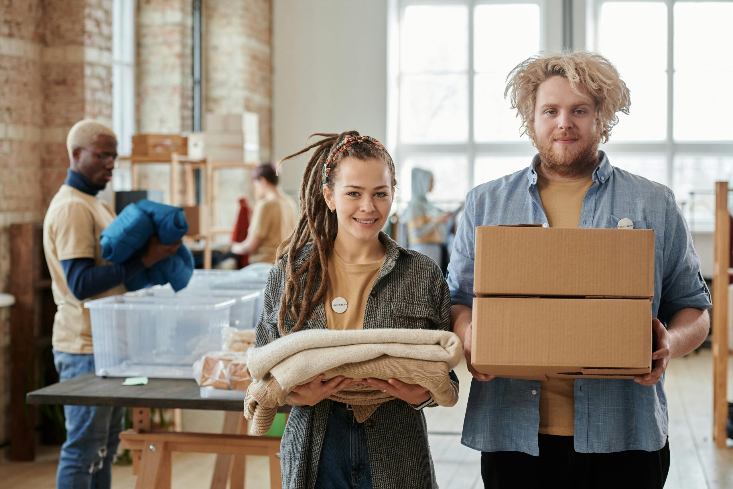Smiling volunteers holding boxes and clothes, assisting in a donation drive indoors.